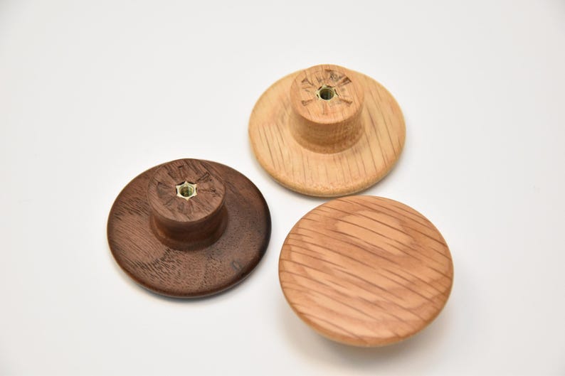 May include: Three wooden knobs in different wood types. The knobs are round and have a flat top. The knobs are all the same size.