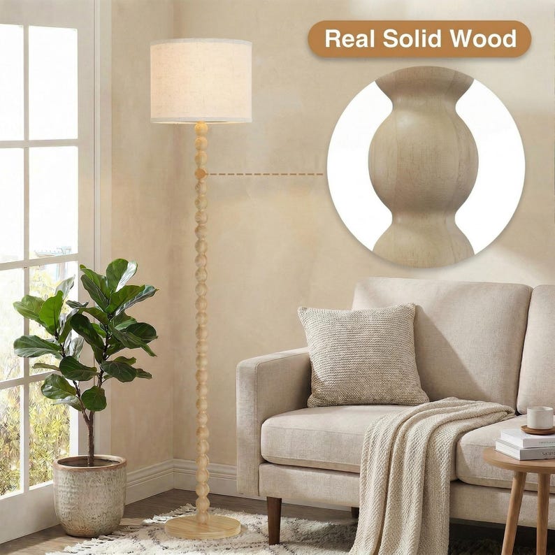 May include: A floor lamp with a light-colored, cylindrical fabric shade and a tall, slender stand composed of stacked wooden spheres. The base is a flat, circular wooden disc. A circular inset highlights the texture of the real solid wood.