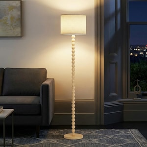 May include: A floor lamp featuring a tall, slender pole constructed from a vertical stack of light-colored wooden spheres. The lamp is topped with a cylindrical, off-white fabric drum shade that emits a warm, soft glow, supported by a circular base.