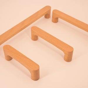 May include: Four wooden cabinet pulls in various sizes. The pulls are all made of light brown wood and have a simple, rounded design.