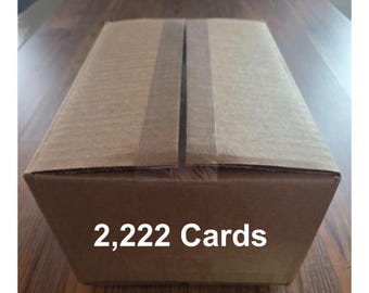 May include: A rectangular cardboard box with the text "2,222 Cards" in white. The box is sealed with tape and sits on a wooden surface. The box is brown.