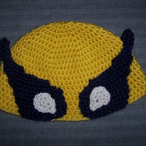 May include: A yellow crocheted beanie with blue and white crocheted accents resembling eyes. The beanie is a handmade item.