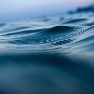 May include: A close-up of ocean water, showing gentle waves and a gradient of blue hues. The water's surface is in focus, revealing subtle textures and reflections. The image evokes a sense of calm and tranquility.