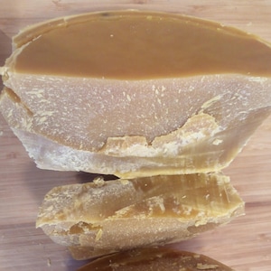 Può includere: Tre blocchi di cera d'api, ognuno con una forma e una dimensione diverse. La cera d'api è di colore giallo chiaro e ha una superficie ruvida e testurizzata.