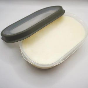 Könnte beinhalten: Ein durchsichtiger Plastikbehälter mit einer weißen Substanz darin. Der Behälter hat einen dunkelgrauen Deckel mit einer Silikondichtung.