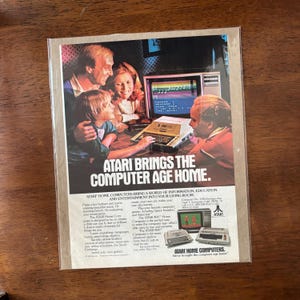 May include: A retro Atari advert showing a family interacting with a computer. The headline reads "ATARI BRINGS THE COMPUTER AGE HOME." The image highlights the Atari 400 and 800 models, promoting home computing for entertainment and education.