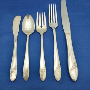 May include: A set of five silver-plated flatware pieces, including a butter knife, a teaspoon, a fork, a dinner fork, and a dinner knife. Each piece features a floral design.
