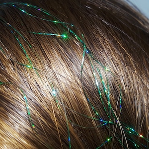 May include: Close-up of brown hair with green and iridescent hair tinsel strands woven in.
