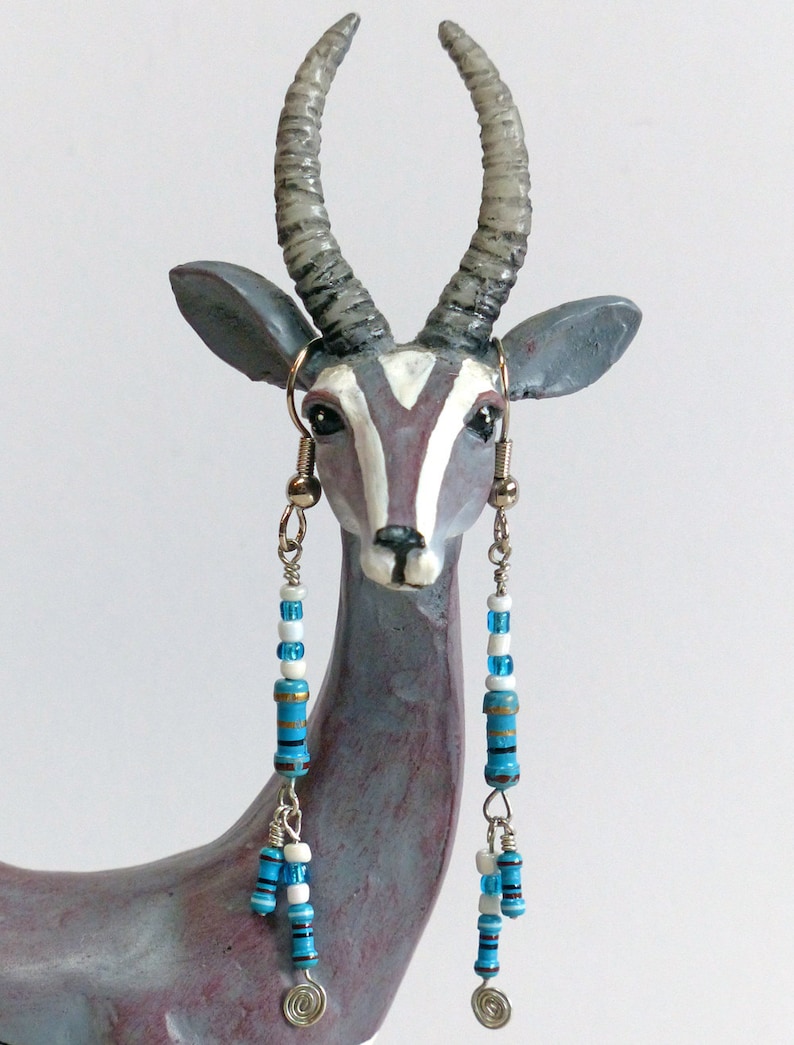 May include: A pair of long, dangling earrings with blue and white beads. The earrings are hanging from the ears of a ceramic animal figurine that resembles an antelope.