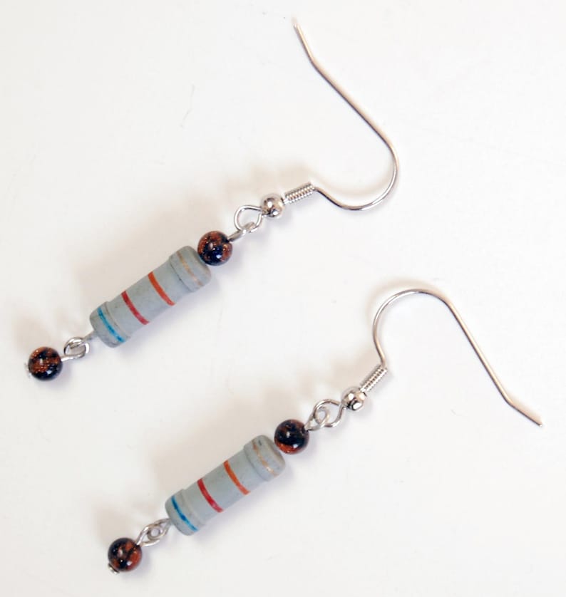 May include: A pair of silver earrings with a gray resistor and brown beads. The resistor has red and blue stripes.