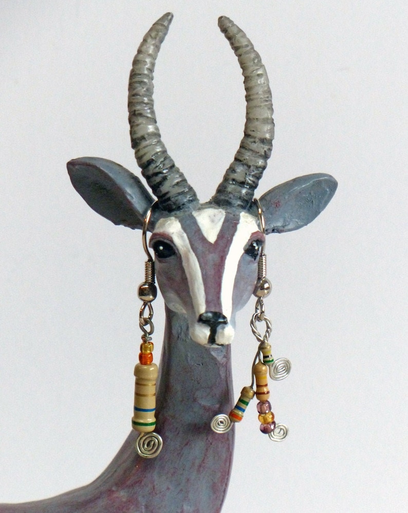 May include: A gray ceramic sculpture of an antelope with long, curved horns. The antelope is wearing earrings with colorful beads and metal accents.