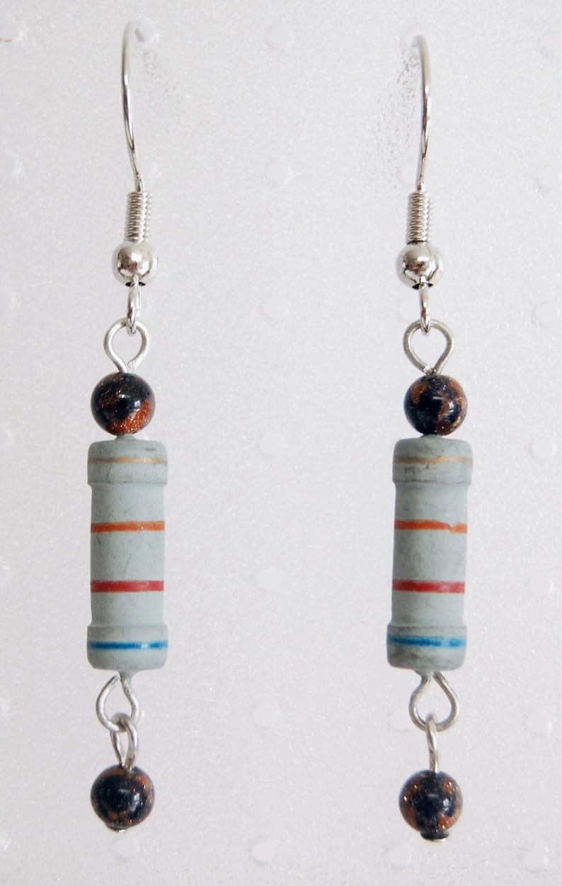May include: A pair of silver earrings with a gray and red resistor charm and a black and copper bead. The earrings are hanging from silver hooks.