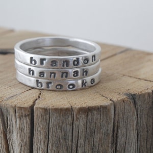 May include: Three silver rings stacked on top of each other. The rings are engraved with the names "Brandon", "Hannah", and "Brooke".