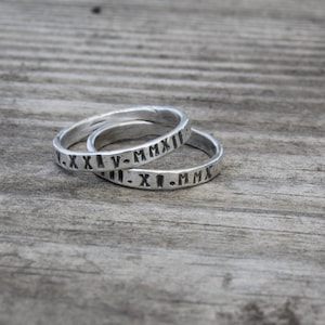 May include: Two silver rings with Roman numeral engravings. The top ring reads "V.XXI.V-MMXII" and the bottom ring reads "II.XI.I-MMXII".
