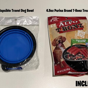Op de afbeelding: Een blauwe, inklapbare reistafel voor honden en een verpakking van 128 gram Purina Alpo T-Bonz hondenbrokken met een afbeelding van een hond en een grill met vlees erop. De verpakking vermeldt "Gemaakt met echt varkensvlees" en "Grote varkensvlees smaak". De tekst "INBEGREPEN" staat in grote letters onderaan de afbeelding.