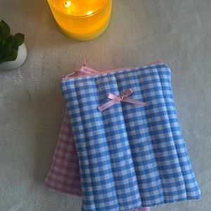Könnte beinhalten: Zwei gesteppte Reißverschlusstaschen mit Gingham-Mustern. Eine Tasche ist rosa und weiß, die andere ist blau und weiß. Beide Taschen haben eine rosa Schleife auf der Vorderseite.