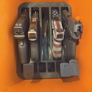 May include: A black foam insert holds four handguns, each in its own compartment. One handgun has a red, white, and blue American flag design. Several black magazines are also visible.