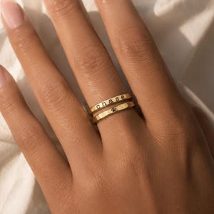 Op de afbeelding: Twee gestapelde ringen van goudkleurig metaal met een gehamerde textuur. De bovenste ring is gegraveerd met de kleine tekst "chase" in een eenvoudig lettertype, terwijl de onderste ring een klein, zwart ingevuld pootafdruk-icoon bevat.
