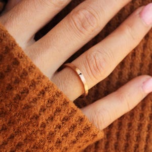 Handmade rose gold ring with a cross engraved in black, worn on the hand of a woman wearing a rust colored sweater.