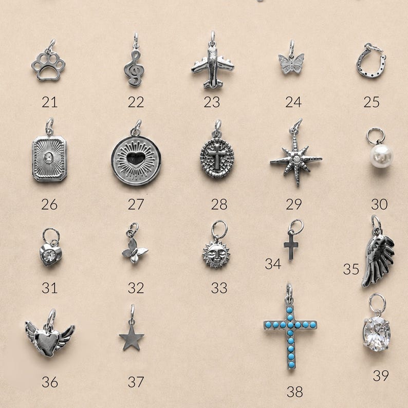 May include: A collection of silver-toned metal charms arranged in a grid, each labeled with a number. The charms include shapes such as a paw print, musical note, airplane, butterfly, horseshoe, heart, cross, star, sun, wing, and a cross with blue stones.