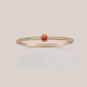 May include: A delicate gold ring with a small, round orange gemstone.