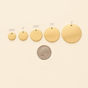 May include: A collection of gold-colored, round metal tags in various sizes, ranging from .375" to 1" in diameter, each with a small hole at the top. A U.S. dime is included for size comparison. The tags are displayed on a cream-colored background.