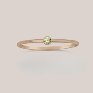 May include: A delicate gold ring with a small, round green gemstone.