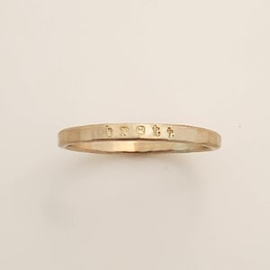 May include: A thin, gold-toned metal band ring with a smooth, polished finish. The exterior surface of the ring features the lowercase name 'brett' stamped clearly into the metal, centered along the front-facing portion of the circular band.