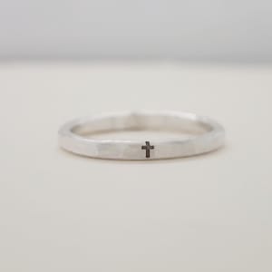 A handmade sterling silver ring, engraved with a black cross, against a white background.
