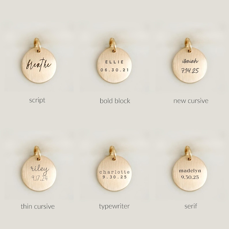 May include: A collection of gold-colored, round pendants with various engraved text styles. Each pendant has a small loop at the top for attachment. The engraved text includes names and dates, such as "breathe," "Ellie 06.30.21," and "Isaiah 7.14.25."