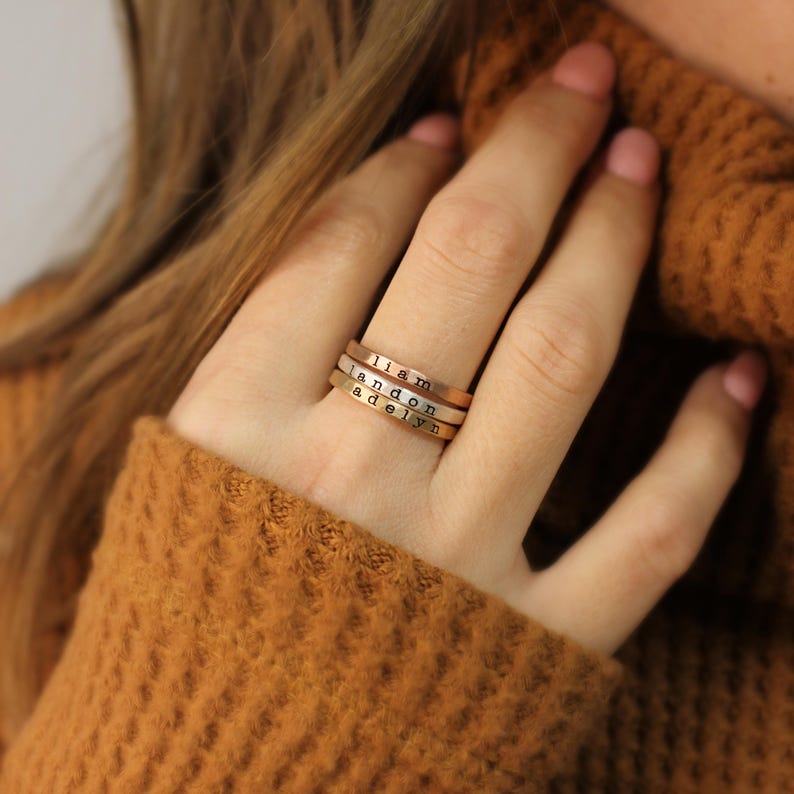 May include: Three stacked gold rings with the names "Liam", "Landon", and "Adelyn" engraved on them.