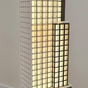 May include: A white and black architectural model of a tall building with a glass facade. The building is lit from within, and the base of the model has the text "250 West 49 Street" inscribed on it.