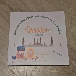 Könnte beinhalten: Ein Ramadan-Arbeitsbuch für Kinder mit dem Titel "Ramadan Mubarak" in orangefarbener Schrift. Das Cover zeigt Illustrationen von lesenden Kindern und eine Moscheen-Silhouette. Text: "30 Hadithe für 30 Tage" und "Ab 6 Jahren".