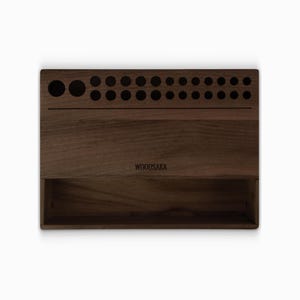 May include: A dark brown wooden organizer with a compartment and a row of holes for storing items. The organizer has the text "WOODSAKA" engraved on the front.