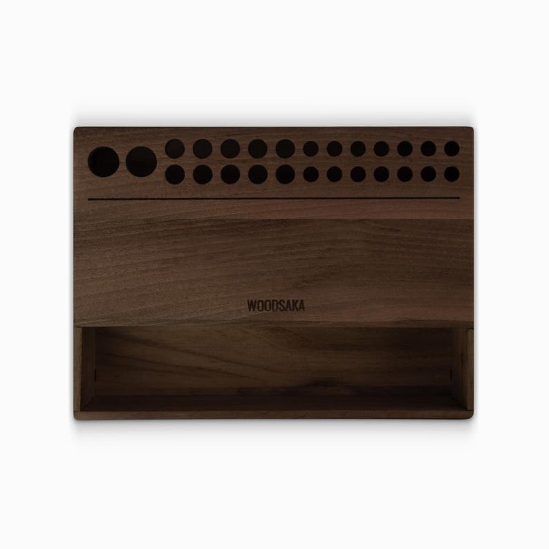 May include: A dark brown wooden organizer with a compartment and a row of holes for storing items. The organizer has the text "WOODSAKA" engraved on the front.