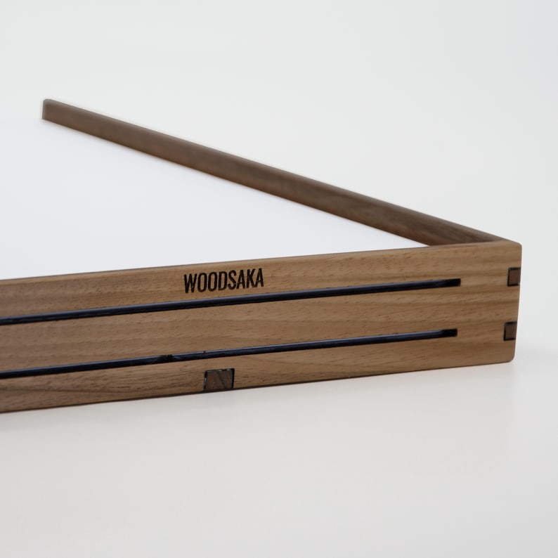 May include: A wooden tray with a dark brown finish and the word "WOODSAKA" engraved on the front. The tray has a simple design with two parallel lines running across the front.