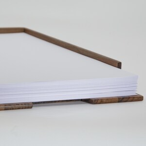 May include: A stack of white paper sheets is held in place by a wooden frame with a natural wood finish.