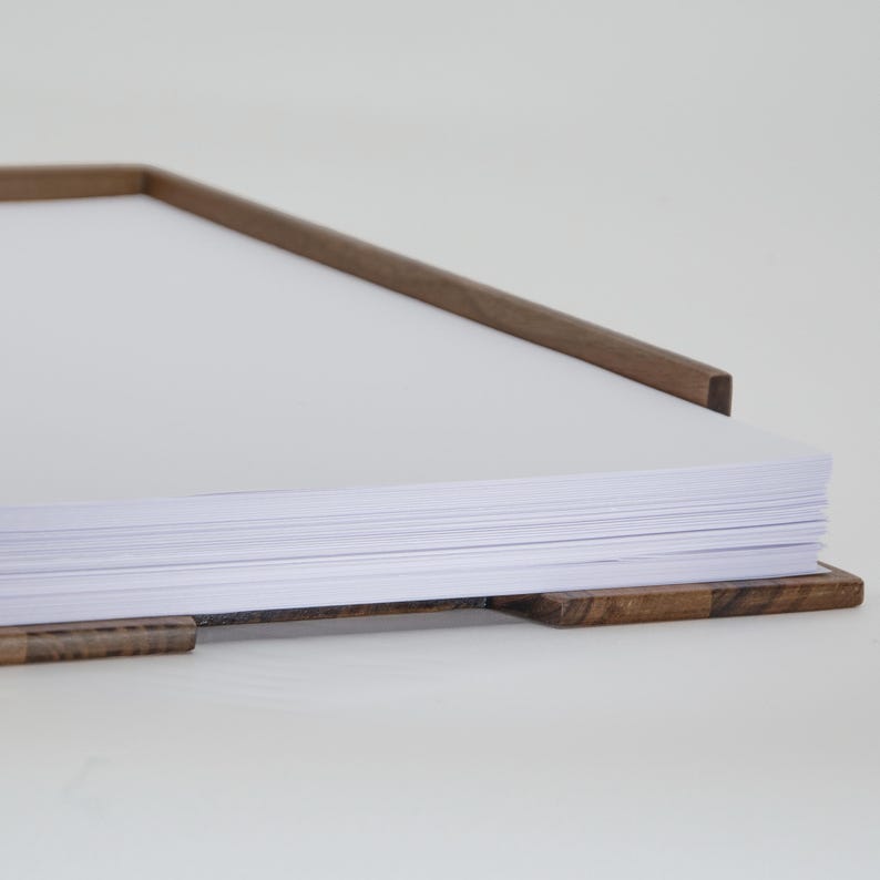 May include: A stack of white paper sheets is held in place by a wooden frame with a natural wood finish.