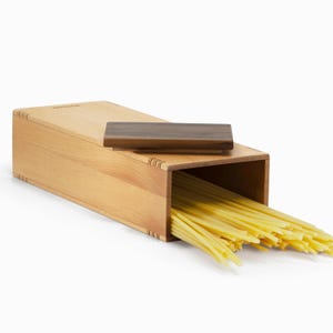 Op de afbeelding: Een houten doos met een walnootkleurig deksel, open om een ​​stapel spaghetti-noedels te laten zien.