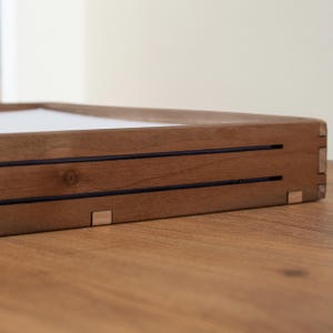 May include: A wooden tray with a light brown finish and two dark brown lines running across the top. The tray has a simple, minimalist design and is perfect for displaying small items.
