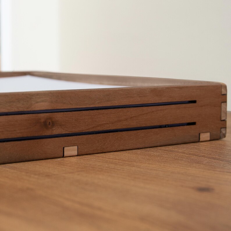 May include: A wooden tray with a light brown finish and two dark brown lines running across the top. The tray has a simple, minimalist design and is perfect for displaying small items.