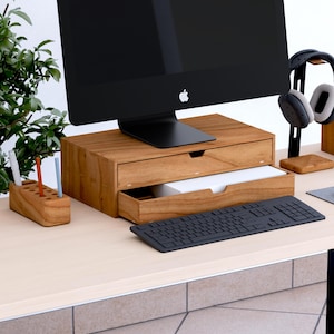 May include: A wooden desk organizer set featuring a monitor stand with a drawer, a pen holder, and a keyboard. The monitor is black, and the desk accessories are made of light brown wood. A pair of headphones rests on a stand.