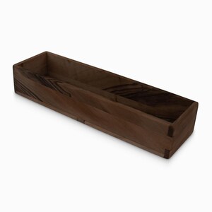 May include: A long, rectangular wooden box with a natural wood finish. The box has a simple design and is perfect for storing small items.