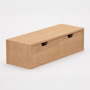 Può includere: Una mensola sospesa in legno chiaro con due cassetti. La mensola è rettangolare con finitura a venatura naturale. Ogni cassetto ha una maniglia incassata. La mensola è progettata per il montaggio a parete.