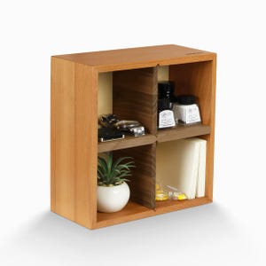 May include: A wooden cube shelf with four compartments. The shelf is made of light brown wood and has a dark brown wood accent. The shelf is filled with various items, including a potted plant, a watch, and ink bottles.