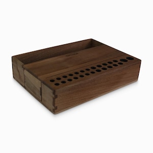 May include: A wooden organizer with a compartment for a phone and a row of holes for storing pens or pencils. The organizer is made of dark wood and has a natural finish.