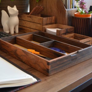 May include: A wooden desk organizer with four compartments. The organizer is made of dark wood with a natural grain pattern. The organizer is labeled "Woodstock".