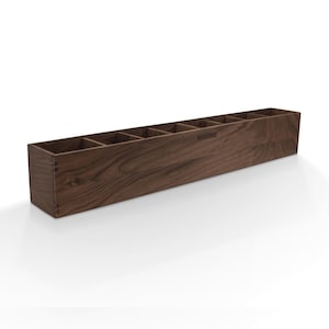 May include: A long, rectangular wooden organizer with seven compartments. The organizer is made of dark brown wood and has the word "WOODISHEK" engraved on the front.