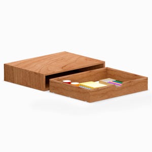 Puede incluir: Un organizador de escritorio de madera con una caja rectangular y una bandeja deslizante. La bandeja contiene pequeños útiles de oficina, incluyendo notas adhesivas de colores y bolígrafos. La madera tiene un tono marrón rojizo cálido.