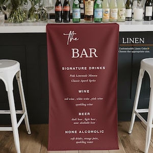 Könnte beinhalten: Ein weinrotes Bar-Schild aus Leinen mit weißem Text, der Getränke, Wein, Bier und alkoholfreie Optionen auflistet. Das Schild wird vor einer Bar mit Flaschen und Gläsern angezeigt. Zwei weiße Hocker befinden sich auf beiden Seiten.